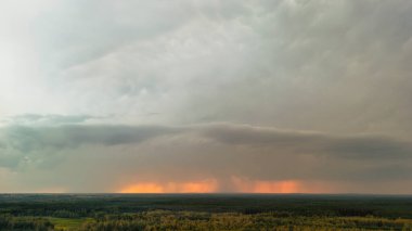 Uçsuz bucaksız yeşil orman manzarasının üzerinde dramatik fırtına bulutları beliriyor. Canlı turuncu ışık renkleri bulutların arasından kırılıyor ve çarpıcı bir kontrastlık yaratıyor. Sahne güzelliği ve gücü yakalar..