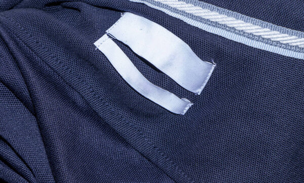 Close-up of fabric with white labels sewn into dark material. Labels and fabric show a texture suitable for textile industry applications and fashion designs.