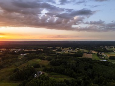 Gün batımında sakin bir kırsal arazinin nefes kesici hava manzarası gökyüzünde canlı renkler ve dağınık evlerle dolu yemyeşil alanlar..