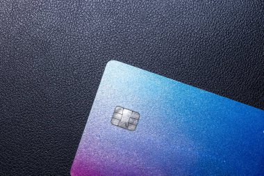 Modern ödeme yöntemlerini ve finansal teknolojiyi vurgulayan desenli siyah bir yüzeye renkli bir kredi kartının yakın çekimi. Finansal ve ticari görseller için ideal.