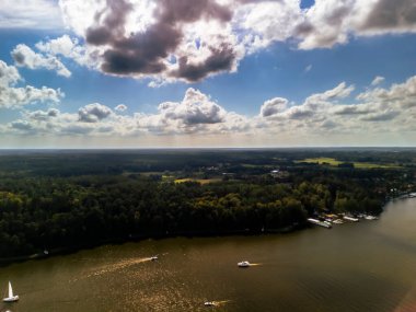 Parçalı bulutlu bir gökyüzünün altındaki gür ormanlarla çevrili sakin bir gölün havadan görünüşü doğa ve seyahat temaları için denizde gezinen tekneleri gösteriyor..