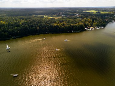 Bereketli ormanlar ve tarlalarla çevrili sakin bir göl üzerinde seyreden teknelerin havadan görüntüsü. Bu cennet manzarası, boş zamanların ve yaz tatillerinin özünü yansıtıyor..