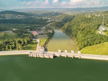 Polonya 'daki Solina Barajı' nın hava görüntüsü rezervuarın etrafındaki yemyeşil yeşilliği gösteriyor. Bu manzaralı manzara, doğanın ve mühendisliğin uyumunu yakalar..