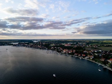 Mikolajki Polonya 'nın hava manzarası, bulutlu bir gökyüzünün altında yemyeşil ve dingin suları olan büyüleyici göl kentini gösteriyor. Seyahat ve manzara ilhamı için ideal..