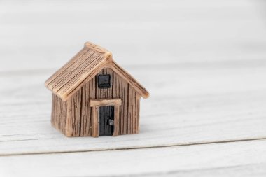 Küçük ahşap bir ev figürü beyaz bir yüzeye oturmuş evi ve barınağı sembolize ediyor. Gayrimenkul kredisi ve konut teması için mükemmel.