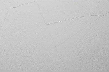 Çatlak beyaz bir duvarın yakın plan görüntüsü dokuyu ve kusurları vurguluyor. Görüntü, arkaplan veya resimsel amaçlar için uygun bir minimalist tasarım yakalar.