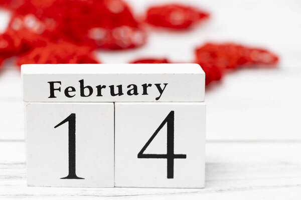 Деревянный календарь, посвященный Дню Святого Валентина, в окружении красных украшений сердца, символизирующих любовь и признательность партнерам и друзьям.