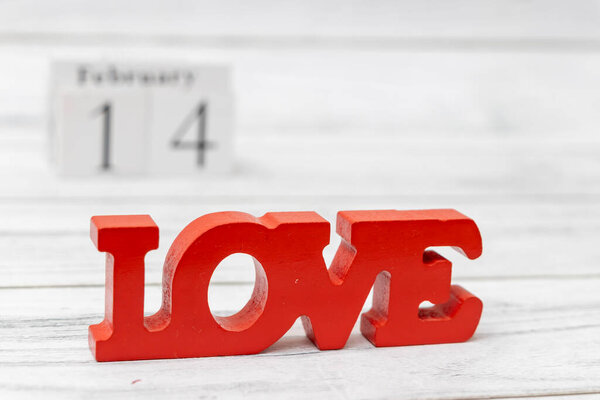 День святого Валентина украшение со словом Любовь жирными красными буквами, установленными на белом деревянном фоне с календарем выделения 14 февраля.