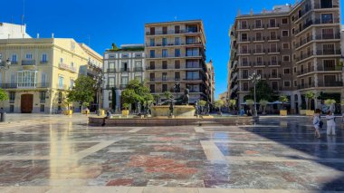 Valencia İspanya - 13 Temmuz 2025: Canlı bir şehir meydanı tarihi mimariyi gözler önüne seriyor bir fıskiye palmiyesi ve güneşli günün tadını çıkaran insanlar seyahat ve kültürel keşifler için ideal.