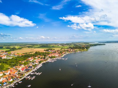 Mikolajki Polonya - 29 Eylül 2024: Mikolajki 'nin deniz kenarı boyunca büyüleyici evler ve gün ortasında gölü çevreleyen yemyeşil manzaralar gösteren hava manzarası.