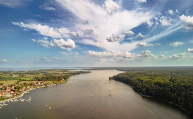Mikolajki Polonya - 29 Eylül 2024: Bereketli yeşil ormanlar ve canlı mavi gökyüzüyle çevrili sakin sularda yüzen yelkenli tekneli göllerin manzarası.
