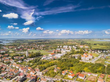 Mikolajki Polonya - 29 Eylül 2024: Berrak mavi gökyüzü altında canlı evler sergilenen yemyeşil ve göllerle çevrili pitoresk bir kasabanın havadan görünüşü.