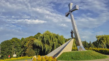 Przemysl Polonya - 12 Eylül 2025: İçinde haç bulunan büyük bir anıt ve yeşil ağaçlardan oluşan bir arka plan ve barışı simgeleyen mavi gökyüzü üzerine kurulmuş bir heykel.