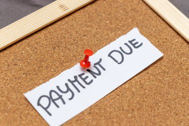 Ödeme bildirimi kırmızı raptiyeli bir mantar panoya tutturulmuş. Not, iş bağlamında sıklıkla kullanılan mali yükümlülükler için bir hatırlatma görevi görüyor.