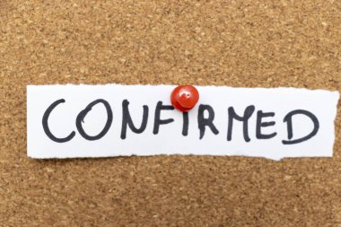 CONFIRMED sözcüğünü gösteren el yazısıyla yazılmış bir not bir mantar panoya tutturulmuş. Not, makam veya kişisel kullanım için uygun bir onay ve onay hissini iletir.