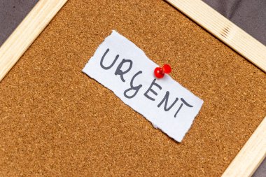 Ofisteki anımsatıcı veya duyurular için uygun önemi ve aciliyeti sembolize eden bir mantar panoya tutturulmuş URGENT sözcüğünü gösteren el yazısıyla yazılmış bir not.