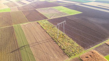 Uçsuz bucaksız tarım alanlarının havadan görünüşü farklı toprak desenleri ve bitki örtüsü sergiliyor. Elektrik hatları kırsal enerji altyapısını sembolize eden araziyle kesişiyor.