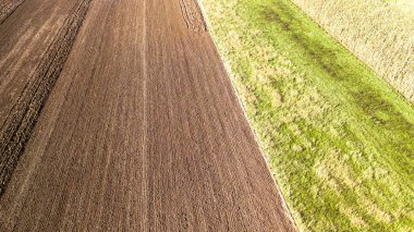 Tarım alanlarının havadan görünüşü zengin kahverengi toprak ve canlı yeşil çimenleri gösteriyor. Bu manzara çiftçilik yöntemlerini ve kırsal bölgelerdeki mevsimsel değişiklikleri vurguluyor.