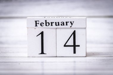 14 Şubat Sevgililer Günü 'nü simgeleyen bir takvim bloğu Sevgi ve kutlama temalarını çağrıştıran hafif ahşap bir arka planla çevrili..