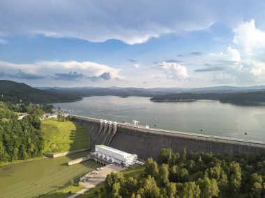 Solina Poland - 29 Haziran 2024: Solina Barajı 'nın havadan görünüşü dağlarla ve nehirle çevrili büyük beton yapısını bulutlu parlak bir gökyüzü altında gösteriyor.