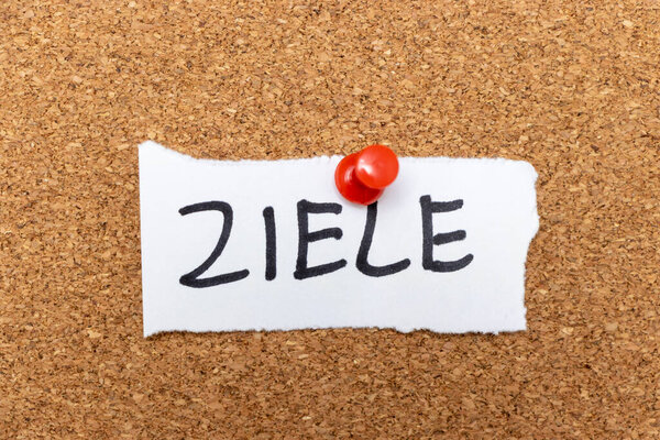 Ручная записка с надписью "ZIELE" прикреплена к пробковой доске. Представляет цели и задачи, часто используемые для личностного развития и мотивации в различных контекстах.