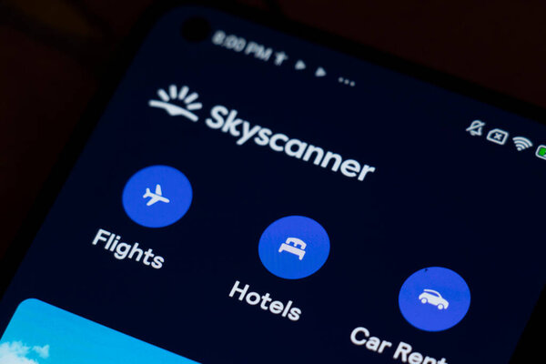 Польша Warsaw - 6 ноября 2025: Закрытие экрана смартфона, показывающего приложение Skyscanner с опциями авиабилетов, отелей и проката автомобилей.