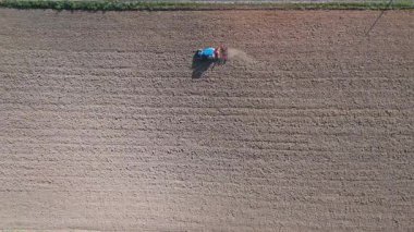 Kırsal alanda yeni sürülmüş bir tarlada çalışan mavi bir traktörün havadan aşağı görüntüsü..