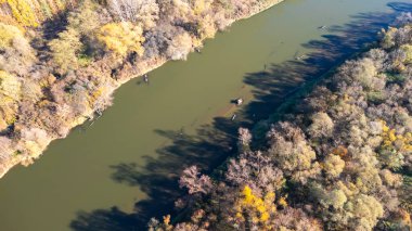 Sonbahar renkli ormanlarda süzülen sakin bir nehrin havadan görünüşü durgun suda yansımalarını gösteriyor. Doğa seyahati ve manzara temaları için ideal.