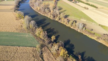Sonbahar boyunca altın tarlalar ve yemyeşil ağaçlarla çevrili dolambaçlı bir nehrin havadan görünüşü. Bu manzaralı manzara sükuneti yakalar ve güzelliği yansıtır..
