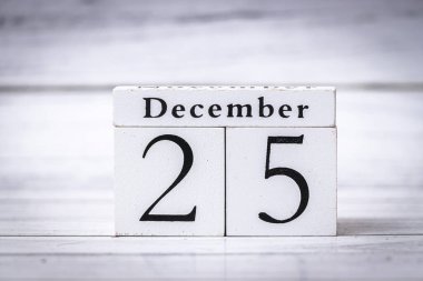 25 Aralık Noel kutlamalarını gösteren ahşap bir takvim. Arka planda minimalist bir tasarım mevsimlik temalar için sıcak ve samimi bir ortam ekliyor.