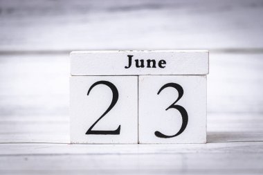 23 Haziran tarihini gösteren bir blok takvimi. Beyaz bloklar, basitlik ve işlevselliği vurgulayan açık ahşap bir zemin ile tezat oluşturuyor. Zaman yönetimi temaları için ideal.