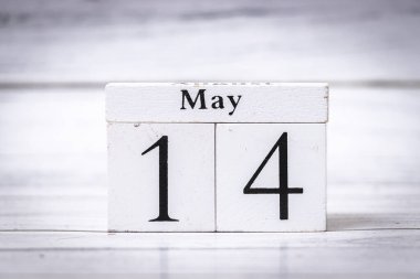 14 Mayıs tarihini gösteren ahşap bir takvim. Beyaz bloklar, zaman yönetimi ve planlamayı sembolize eden bulanık arkaplan karşıtlığına karşıt.