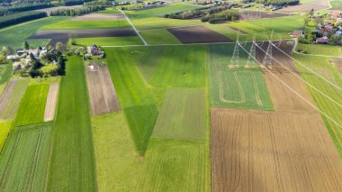 Çeşitli yeşil ve kahverengi tarlaları olan yemyeşil tarım arazilerinin havadan görünüşü. Elektrik hatları, tarımsal güzellik ve kırsal yaşamı gösteren manzara ile kesişiyor. Çevresel temalar için ideal.