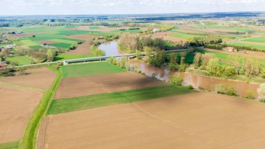 Bereketli tarlalar ve açık gökyüzü altında doğa ve manzara projeleri için ideal tarım arazileri sergilenen dolambaçlı bir nehrin yanındaki yeşil tarım arazisinin havadan görünüşü..
