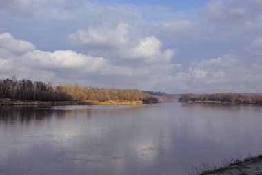 Etrafı ağaçlarla çevrili bulutlu bir gökyüzünün altında sakin bir nehir yavaşça akar. Sönük renkler doğa meraklıları için ideal bir ortam yaratıyor..