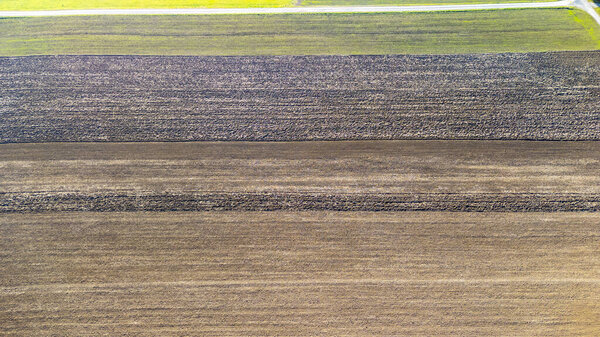 Воздушный вид сельскохозяйственных полей, демонстрирующих лоскутное полотно пашни и зеленых культур. Изображение отражает суть сельских ландшафтов и сезонные изменения.