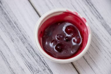 Ahşap arka planda beyaz bir kasede kremalı kızılcık sosunun yakın plan görüntüsü. Bu zengin çeşni, tat ve renk katan şenlikli yemekler ve tatlılar için mükemmeldir..