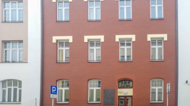 Rzeszow Polonya - 16 Kasım 2025: Birden fazla penceresi ve şehir mimarisi ve modern tasarımı gösteren bir park levhası olan tuğla binanın önü.