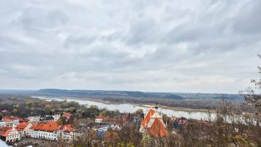 Kazimierz Dolny Polonya - 11 Kasım 2025: Bulutlu gökyüzü ile Kazimierz Dolny 'nin manzarası mimari ve Vistula Nehri manzarasını sergiliyor. Turizm tanıtımı için ideal.