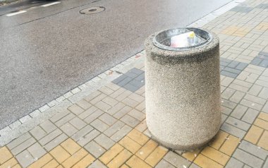 Şehir kaldırımındaki beton bir çöp tenekesi, kamu alanlarındaki kentsel atık yönetimi ve çevresel kaygıları kısmen ön plana çıkarıyor.