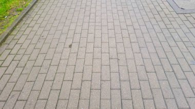 Gri tuğlalı kaldırımın yakın plan görüntüsü kentsel bir ortamda iyi korunan bir yürüyüş yolunu gösteriyor. Düzenlemeler şehir manzaraları için modern bir estetik ideal yaratıyor..