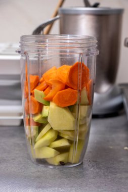 Modern bir mutfakta harmanlanmaya hazır yeşil elma ve havuç da dahil olmak üzere doğranmış meyve ve sebzelerle dolu bir blender kabı. Sağlıklı yemek hazırlama konsepti.