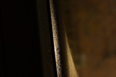 Islak bir pencereye yakın çekim yaparak damlacıkları ve yumuşak bir ışık dağılımını göstererek kasvetli bir atmosfer yaratarak yalnızlık ve yansıma hissi uyandırır..