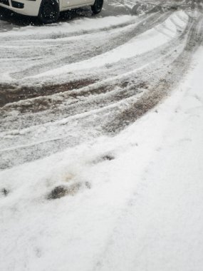 Karla kaplı zemin, kış otoparkında kirli bir arazinin yanında bir lastik izi gösteriyor. Karışık dokular soğuk aylardaki mevsimsel havayı yansıtıyor.