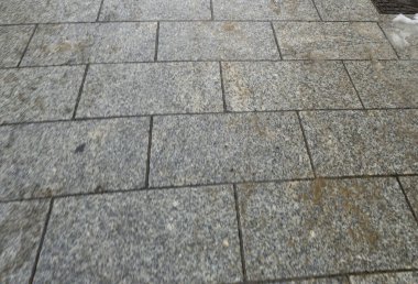 Çeşitli desenleri ve renkleri gösteren gri desenli taş kaldırıma yakın plan. Yüzey son zamanlarda yağmurun yağdığını gösteriyor. Mimari veya kentsel temalar için ideal.