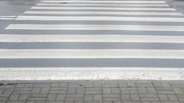 Gri asfalt üzerinde soluk beyaz şeritlerin yer aldığı yaya geçidine yakın çekim görüntüsü bir metropolitan alanındaki kentsel yaşam ve trafik güvenliği tedbirlerini yakalıyor.
