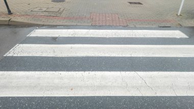 Şehir caddesinde kırık bir yaya geçidinin yakın görüntüsü. Beyaz çizgiler, güvenlik için kentsel altyapının altını çizen gri kaldırımla tezat oluşturuyor.