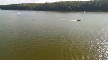Editör sahnesi, Masuria 'nın sularındaki canlı aktiviteleri, Mikolajki, sakin bir gökyüzü altında yüzen yelkenli ve motorlu botları ve yemyeşil alanları yakalar..