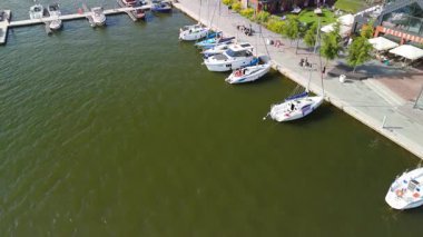 Mikolajki, Polonya, 9 Ağustos 2024: Rıhtım boyunca yanaşan tekneler ve limandan ayrılan bir tekne ile dolu bir marina sahnesi, canlı liman faaliyetlerini gösteriyor