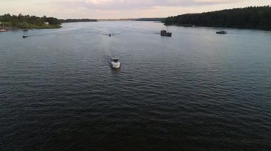 Mikolajki, Polonya, 9 Ağustos 2024: Birden fazla yelkenlinin olduğu sakin bir göl manzarası. Akşam gökyüzü, tekneler sahnenin sükunetini artırmak için yumuşak dalgalar yaratırken suya yansıyor.